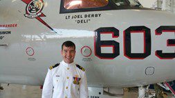 Heidi's son Joel Derby standing in his Naval uniform in front of fighter jet.
