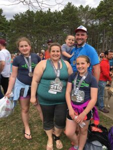 Curtis Deprey with his Wife Jenna Deprey and their two kids smiling after participating in the Eau Claire marathon.