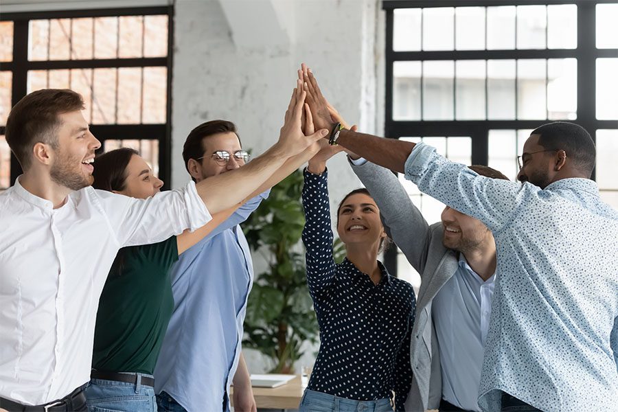 About Our Agency - Cheerful Group of Coworkers Putting Their Hands Together to Celebrate Success in the Office