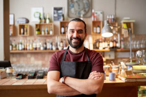 Small business owner smiling in a black apron and maroon t-shirt with his arms crossed after acquiring business insurance.