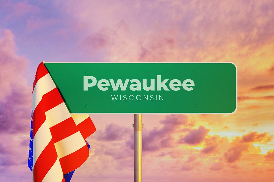 Pewaukee Wisconsin road sign draped in an American flag with a pink sunset in the background.