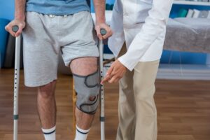 Wisconsin worker in crutches with a knee brace working with a doctor to put pressure on his leg.