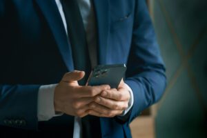 Businessman in navy blue suit using his phone to contact business where an identity thief visited.