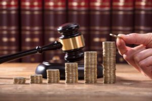 Close-up of human hand stacking 6 stacks of coins in ascending order in front of a judge's gavel.