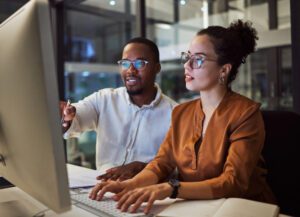 Insurance agency owner pointing at computer screen training a new female agent on providing online administrative services.