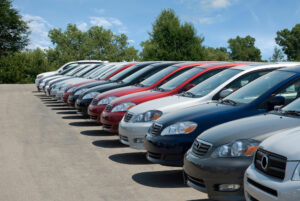 Vehicles lined up at a used car dealership on a sunny day.
