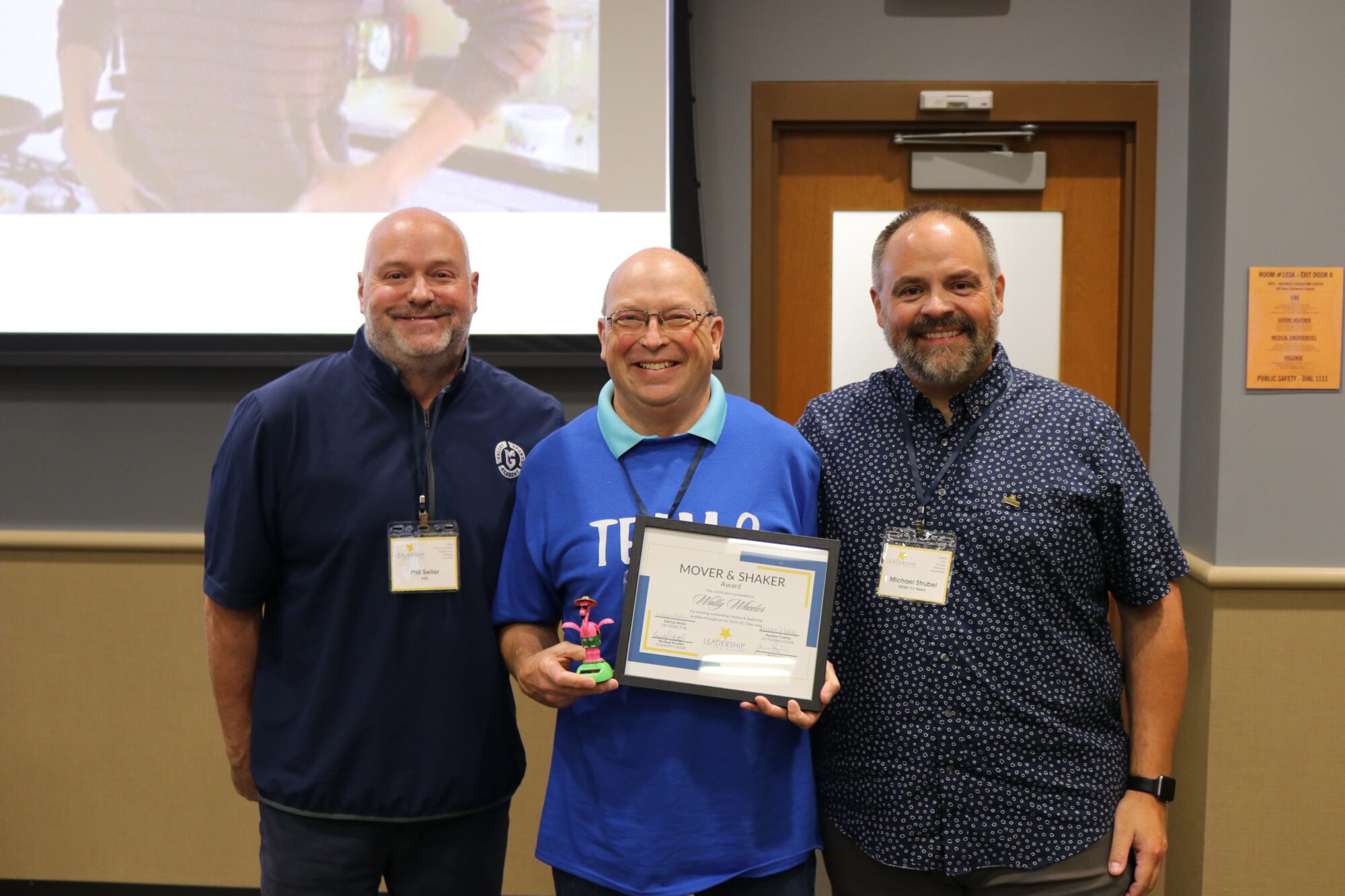 Wally Wheeler holding the Mover & Shaker Award for Leadership Eau Claire Class of 2024 standing next to Phil Swiler of VSA and Michael Strubel of WEAU 13 News.